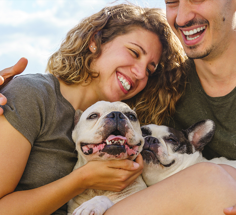 Couple smiling and sitting with dogs outside
