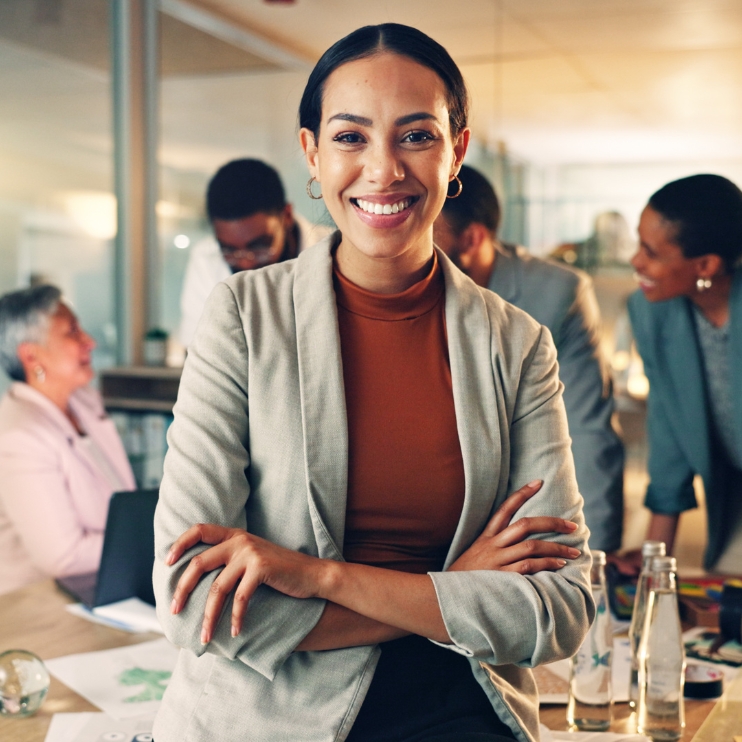 A woman standing in an office, with coworkers in the background.