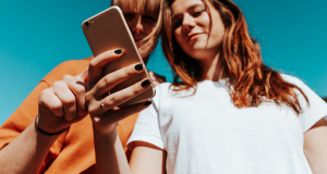 Two people standing next to each other outside looking at a phone.
